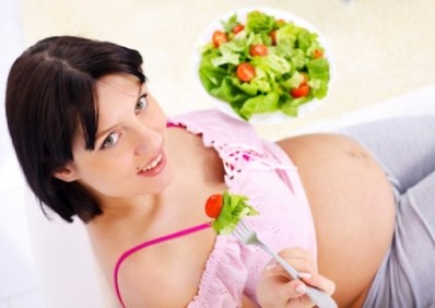 Portrait of a pretty pregnant woman eating vegetable salad, looking upwards.